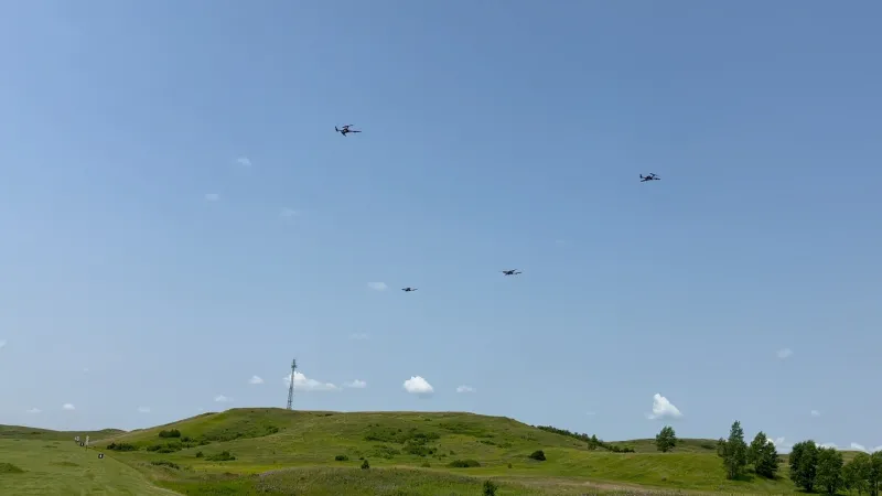 Several drones flying in the sky over green field with some trees.