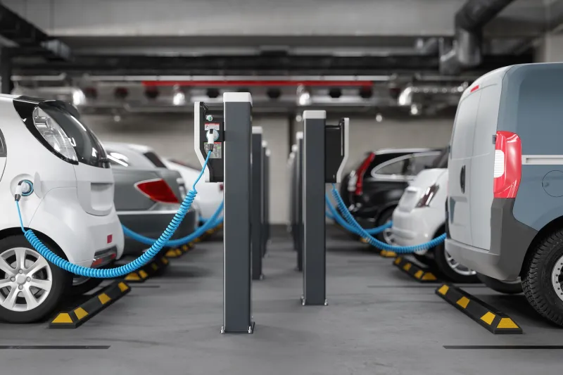 A parking garage setting with electric vehicle charging stations at center and charging vehicles at left and right.