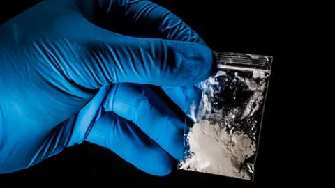 A hand in blue gloves holding a small bag with white powder inside it.